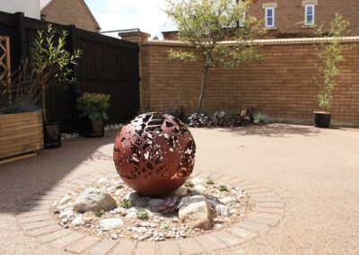 Courtyard planting design with a steel globe fire pit and ornamental grasses.
