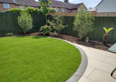 A circular garden lawn framed with blue engineering bricks acts as a mowing strip around the lawn.